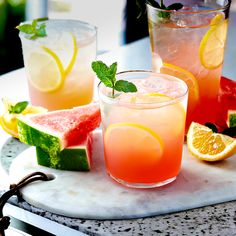 three glasses filled with watermelon and lemonade on a marble tray next to slices of watermelon