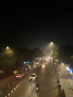 cars are driving down the street at night time, with fog coming from nearby lights