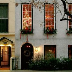 a white building with christmas lights on it's windows and trees in the window boxes