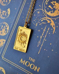 the sun and moon pendant is sitting on top of a blue book with gold foil