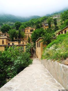 a stone walkway leading up to some buildings on a hill with trees in the background