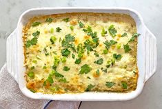 a casserole dish with cheese and green onions in it on a white towel