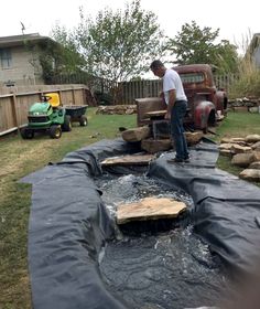 a man standing on top of a black tarp next to an old pickup truck