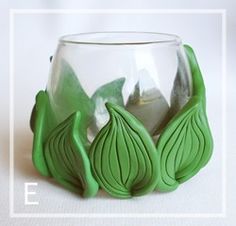 a glass vase with green leaves on the inside and bottom, sitting on a white surface