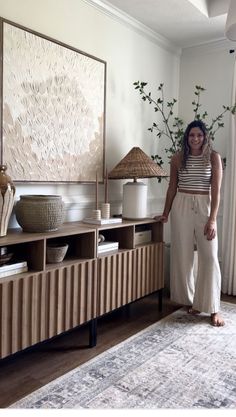 a woman standing in front of a large painting next to a table with vases on it