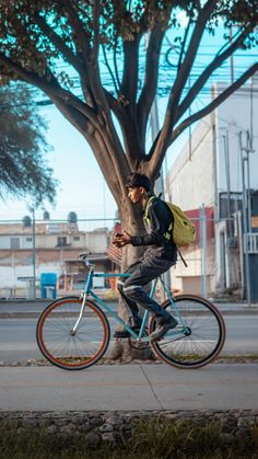 a man riding a blue bike down a street next to a tree and grass covered sidewalk