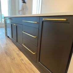 an empty kitchen with black cabinets and gold pulls on the doors, along with wood flooring