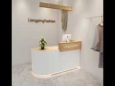 a white reception counter with a plant on it in front of a hanging fashion sign