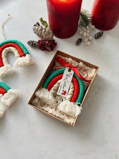 two red and green christmas wreaths in a box next to some candles on a table