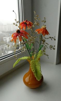 an orange vase filled with flowers on top of a window sill