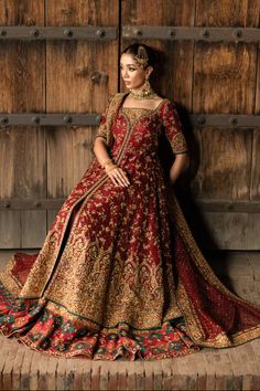 a woman in a red and gold dress standing against a wooden wall with her hands on her hips