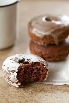 two glazed donuts sitting on top of a piece of paper next to a cup