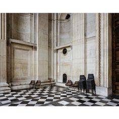 four chairs are lined up in the middle of a checkered floored room with columns