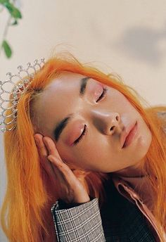 a woman with orange hair wearing a tiara and looking down at her face while holding her hand on her cheek