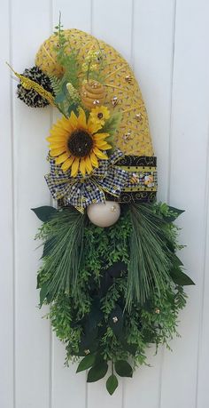 a yellow hat with sunflowers is hanging on a white wall next to greenery