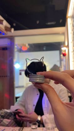 a person holding up a small toy cat on top of a tin can at a table