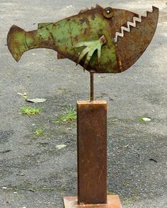 a rusted metal fish sculpture sitting on top of a wooden block