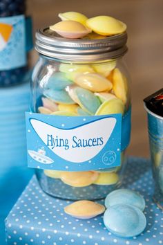 a jar filled with jelly beans sitting on top of a blue table cloth next to two cups