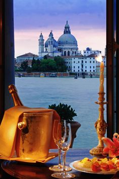 a table with food and wine on it in front of a window overlooking the water