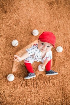 a little boy in a baseball uniform is playing with some balls on the ground and sand