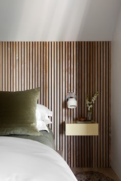 a bed with white sheets and pillows next to a wooden headboard on the wall