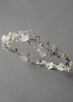 a tiara with white flowers and leaves on the headpiece is shown against a gray background