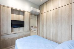 a bed sitting in a bedroom next to wooden cupboards and a tv mounted on the wall