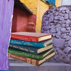 a stack of books sitting on top of a table next to a purple vase and building