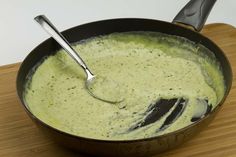 a pan filled with green sauce sitting on top of a wooden table next to a spoon