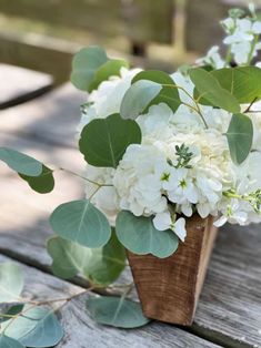 white flowers and greenery in a wooden vase on a picnic table with wood planks