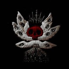 a black background with white feathers and a red skull on it's face in the center