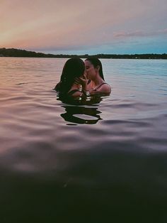 two women are kissing in the water at sunset or dawn, with one woman's face partially hidden by her chest