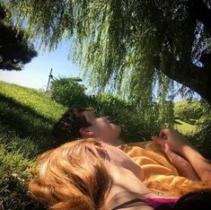 two people laying in the grass under a tree with their eyes closed and one person sleeping