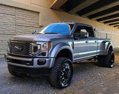 a silver truck is parked in front of a brick wall and under a concrete bridge