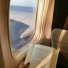 someone is reading a book while flying in an airplane and looking out the window at the ocean