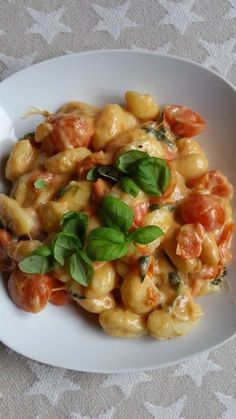 a white plate topped with pasta covered in tomato sauce and spinach garnish