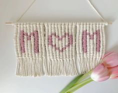 a pink and white wall hanging with the word love on it next to a tulip