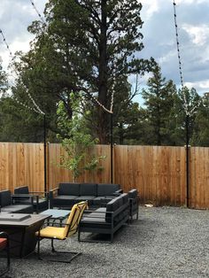 an outdoor seating area in front of a wooden fence with string lights hanging from it