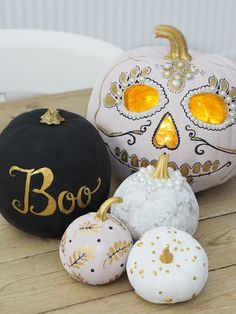 three decorated pumpkins sitting on top of a wooden table next to a black and white pumpkin