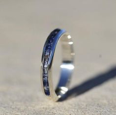 a silver ring with blue and white speckles sitting on the ground next to a shadow