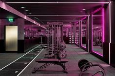 an empty gym with purple lighting in the ceiling and rows of exercise equipment on the floor