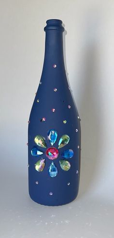 a blue vase with colorful jewels on the top and bottom, sitting against a white background