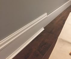 the corner of a room with white trim and wood flooring next to a roll of toilet paper