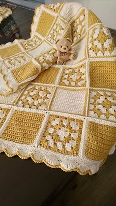 a teddy bear sitting on top of a crocheted blanket with yellow and white squares