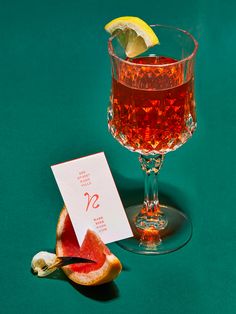 a glass filled with liquid next to a slice of watermelon and a lemon wedge