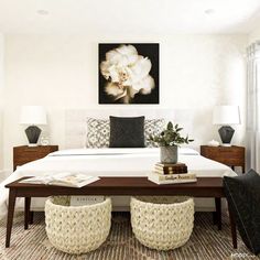 a white bed sitting in a bedroom next to two chairs and a painting on the wall