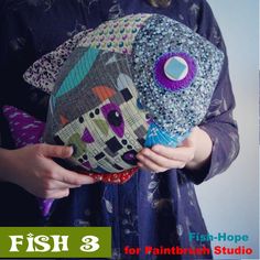 a woman holding a fish shaped pillow in her hands with the words fish hope for paintbrush studio on it