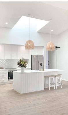 an open kitchen with white cabinets and counter tops, two pendant lights over the island