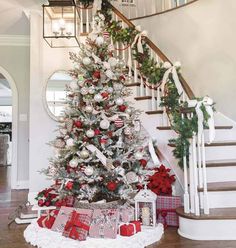 a decorated christmas tree with presents under the banister and stairs in a foyer area