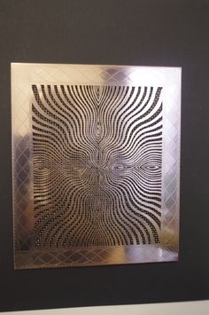 an intricate metal artwork is displayed in a black and silver frame on a white wall